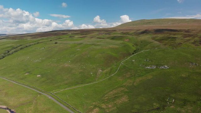Panning right, high-altitude aerial shot of Barbon Beck, Carnforth, Lancashire, England. This stunning countryside features a stream running alongside a small country lane.