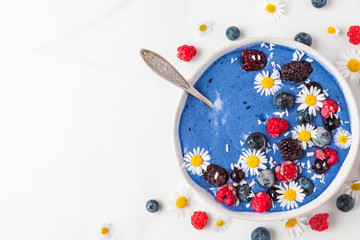 healthy breakfast diet dessert. smoothie bowl made of blue spirulina, frozen banana, berries and coconut with flowers