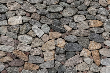 Textured fragment of the granite stone brown-gray facade of the wall
