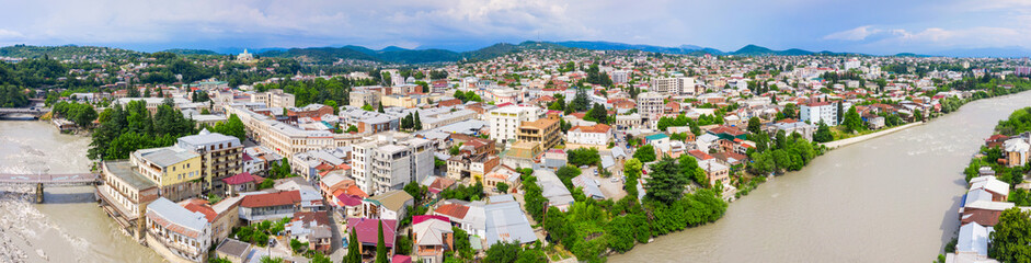 Fototapeta na wymiar Panoramic summer view of the city of Kutaisi, Georgia. Blue sky with clouds. River Rioni and old houses with Red roofs. Mountains in the distance.