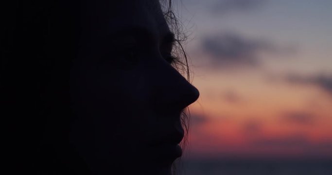 Close up side view of female face silhouetted by sunset evening light on colorful sky background. Macro portrait of young woman looking aside outdoors copy space. Emotion problem depression concept