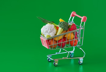 Grocery shopping cart with fresh vegetables and fruits. Isolated on green background. Free GMO....