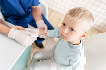 Doctor in blue uniform make elastic bandaged around a boy hand with trauma in his arm. in the hospital