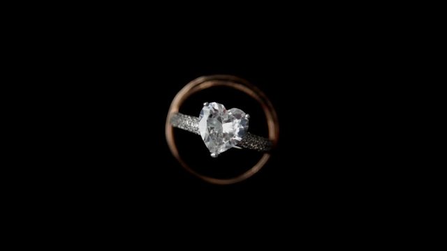 Camera circulating around heart shape wedding ring on dark background close up