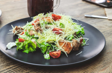 Healthy Grilled Chicken Caesar Salad with Cheese and Croutons on black plate. Selective focus