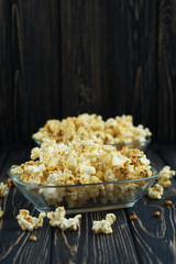 Homemade vegan fresh crunchy salted popcorn in a glass plate on a dark wooden table. A useful snack for a movie, an idea for a meal. Dark mood vertical, place for text background.