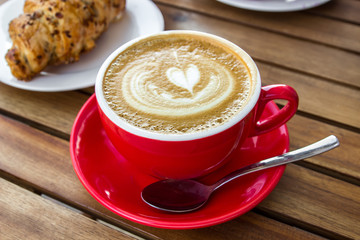 Red cup of cappuccino with croissant on a table in an outdoor cafe. Tipical italian breakfast. Selective focus