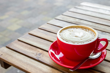 Red cup of cappuccino with croissant on a table in an outdoor cafe. Tipical italian breakfast....