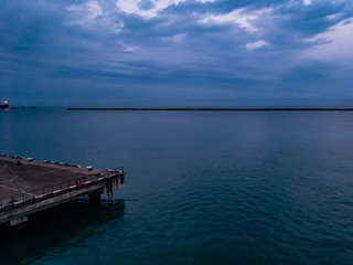 Fototapeta na wymiar Sea pier in the summer morning surrounded by green sea water and with dark clouds on the horizon.