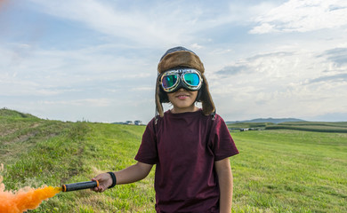 Little boy plays with colored smoke, wearing a 1920s aviator hat and airplane pilot glasses