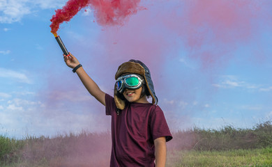 Little boy plays with colored smoke, wearing a 1920s aviator hat and airplane pilot glasses
