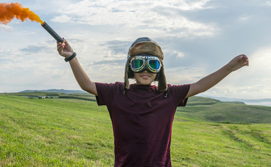 Little boy plays with colored smoke, wearing a 1920s aviator hat and airplane pilot glasses