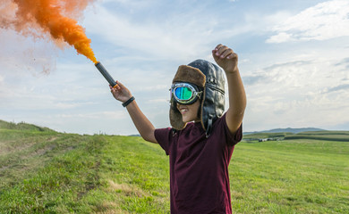 Little boy plays with colored smoke, wearing a 1920s aviator hat and airplane pilot glasses