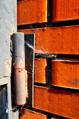 Old rusty door hinge with a spider web on a red brick wall.