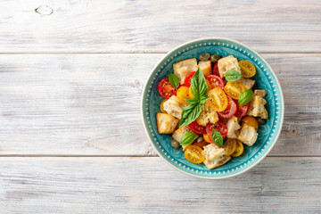Traditional Italian salad Panzanella with cherry tomatoes, bread, capers and basil in bowl on wooden table. Top view. Copy space.