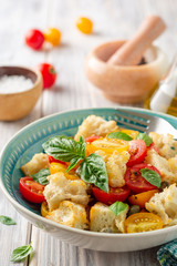 Traditional Italian salad Panzanella with cherry tomatoes, bread, capers and basil in bowl on wooden table. Selective focus.