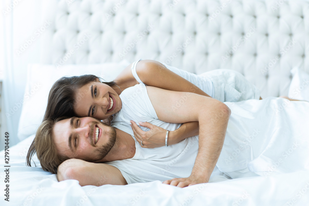 Wall mural Young happy couple lying together in bed.