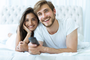 happy couple with remote lying in bed at home and watching tv.