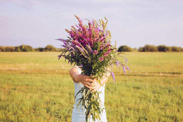 The girl covering her face with a bouquet of wild flowers