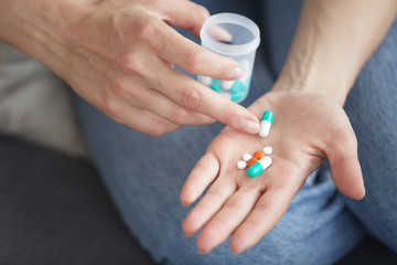 Close-up of unrecognizable woman holding drug bottle and counting pills on palm