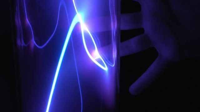 Child's hand touches the plasma tube with a dark blue lightning in the dark. Exhibition at the Museum of cosmonautics.