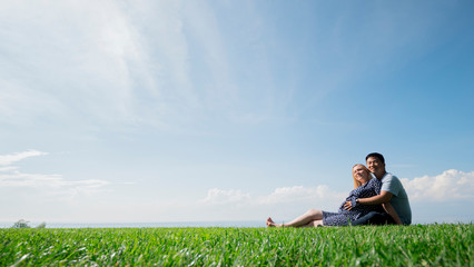 Asian man with a pregnant woman are resting in nature in a picturesque place, sit on the green grass