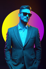Obraz premium Young handsome model posing in a studio in a trendy neon light. Fashionable man in a stylish suit. Vibrant color. Bright colorful light effects. Disco style. Overlay. Gel filter. Supersaturated
