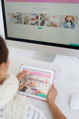 Close-up of woman sitting in front of computer with medical analysis pictures and using tablet...