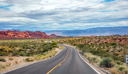 Long winding highway with ups and downs, cloudy blue sky. Valley of Fire Nevada, USA