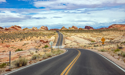Long winding highway with ups and downs, cloudy blue sky. Valley of Fire Nevada, USA