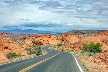Fototapeta na wymiar Long winding highway with ups and downs, cloudy blue sky. Valley of Fire Nevada, USA