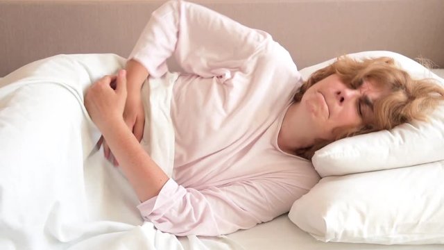 Mature woman with stomachache lying in bed holding her stomach