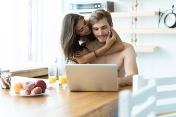 Couple in front laptop computer in the kitchen.