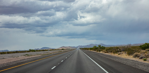 Naklejka premium Long highway in the american desert, cloudy blue sky