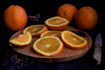 Halves and whole oranges on wooden board over black background, close up