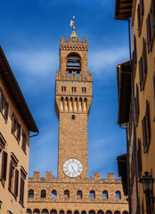Palazzo Vecchio (Old Palace) clocktower, the beautiful Florence town hall erected in the 14th century and  designed by the famous medieval architect Arnolfo di Cambio, seen from a narrow street 