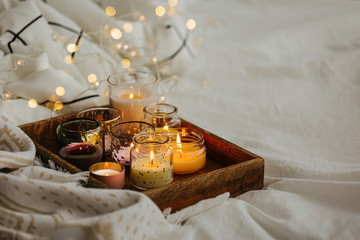 Burning candles on wooden tray with warm plaid in bed.  Scandinavian style. Hygge concept.