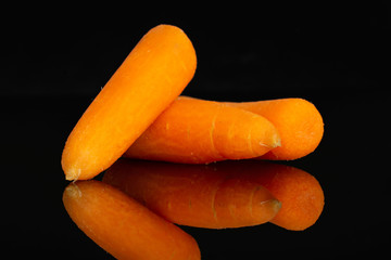 Group of three whole peeled orange baby cut carrot isolated on black glass