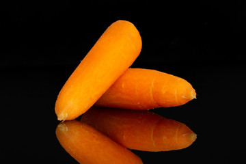 Group of two whole fresh peeled orange baby cut carrot isolated on black glass