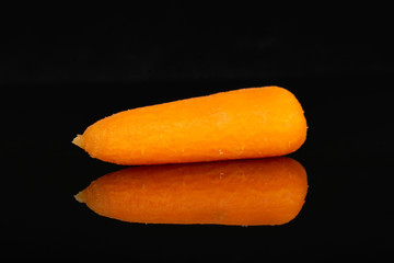 One whole peeled orange baby cut carrot isolated on black glass
