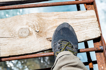 Top view foot in hiking shoe on wooden bridge over river