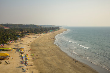 Arambol, Goa/India - 04.01.2019: people walk along the sandy beach of the sea and swim in the ocean against the backdrop of palm jungle, aerial view