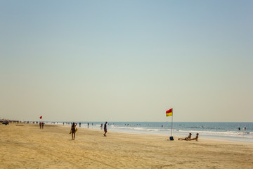 Arambol, Goa/India - 04.01.2019: sandy coast of the ocean coast with walking and bathing people and a lifeguard flag