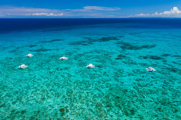 Aerial view of traditional Bangka boats moored above a large tropical coral reef in a calm ocean (Malapascua, Philippines)