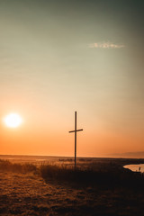 Concept conceptual black cross religion symbol silhouette in grass over sunset or sunrise sky, Resurrection of Jesus, Cross christian