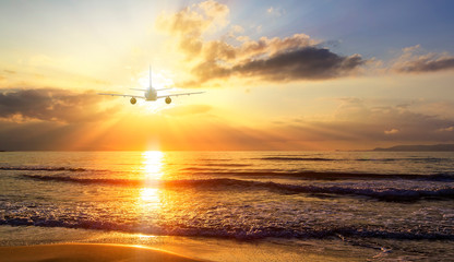 Airplane flying over blur tropical beach bokeh sun light wave and sunset sky abstract background....
