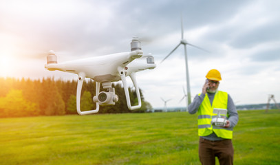 Drone operated by construction worker inspecting wind turbine, flying with drone.