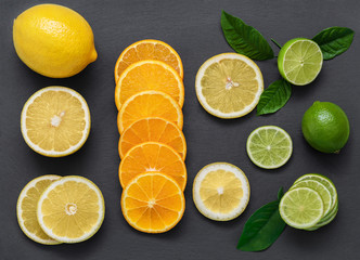 Naklejka na ściany i meble Sliced citrus fruit on a stone table. Juicy ripe slices of orange, lemon and lime on a black background. Fruit mix, top view close-up.