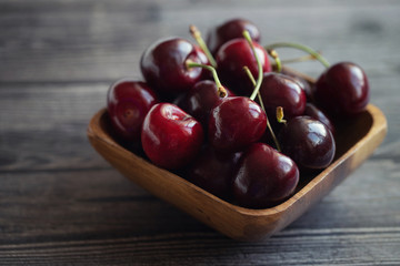 Ripe fresh cherries in a wooden bowl. Food background. Red juicy cherry berry on grey wooden background. Cherries in a dish close-up.