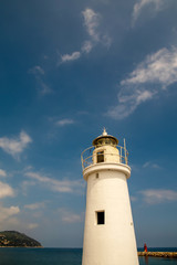 Fototapeta na wymiar Low angle vertical view of a white lighthouse with a cape in the background against blue sky and sea in a sunny summer day, Porto Maurizio, Imperia, Liguria, Italy